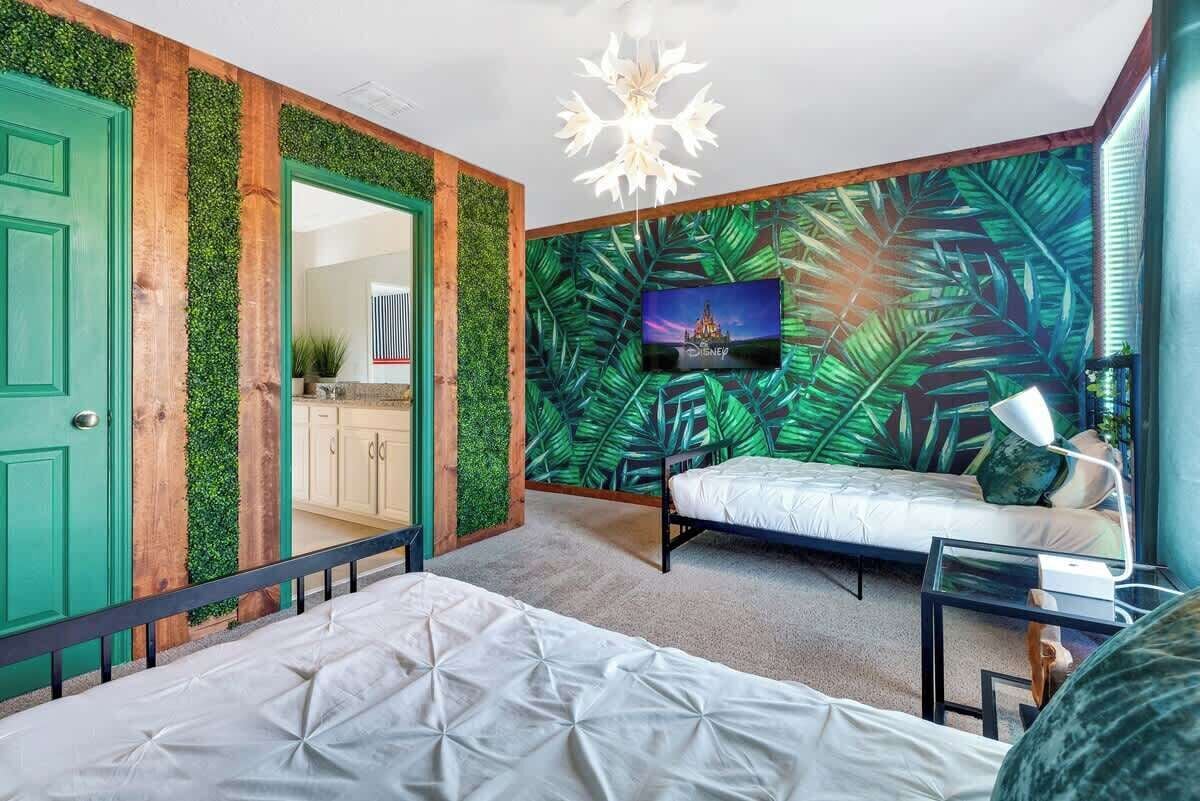 Une chambre avec un lit, un téléviseur et un mur décoré d’un motif de feuilles vertes.