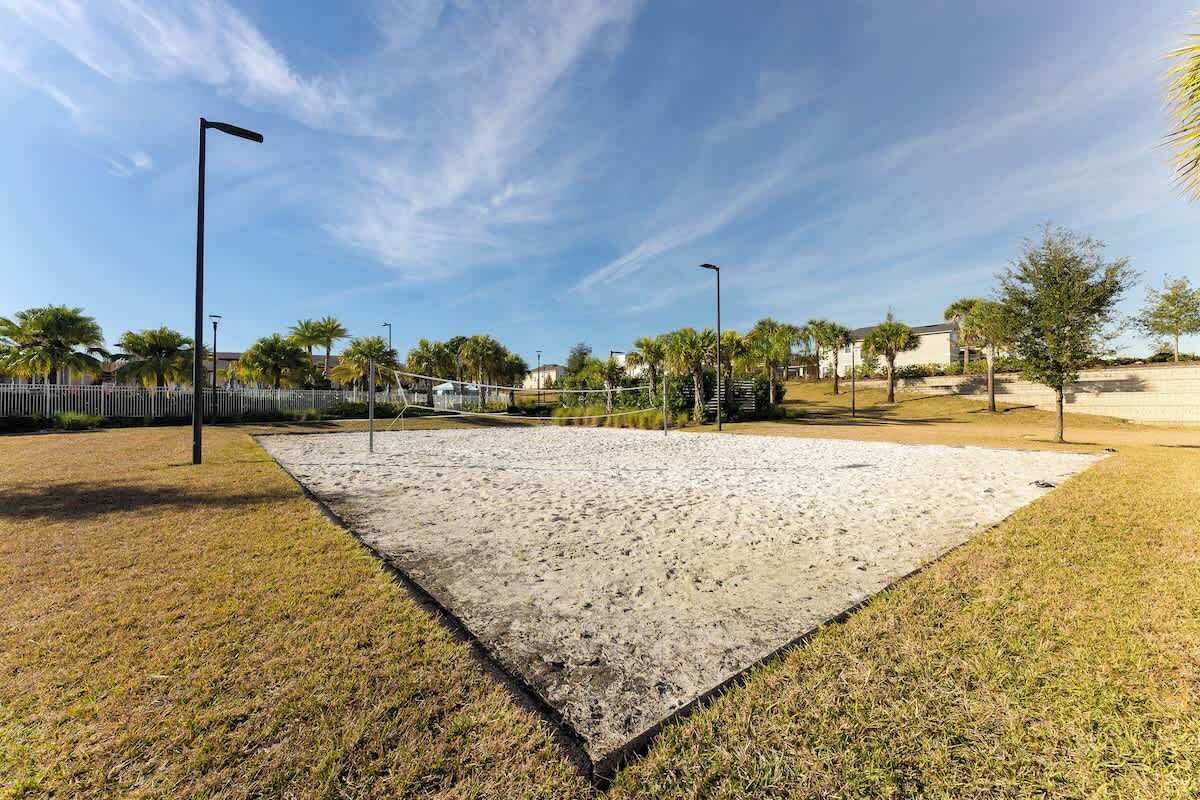 A sandy area with a fence, street lamps, and palm trees.