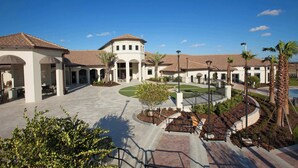 A spacious courtyard with a central fountain, surrounded by palm trees and a white building with arched walkways. - Stylish 5BR Home With Themed Bedrooms (Kissimmee)