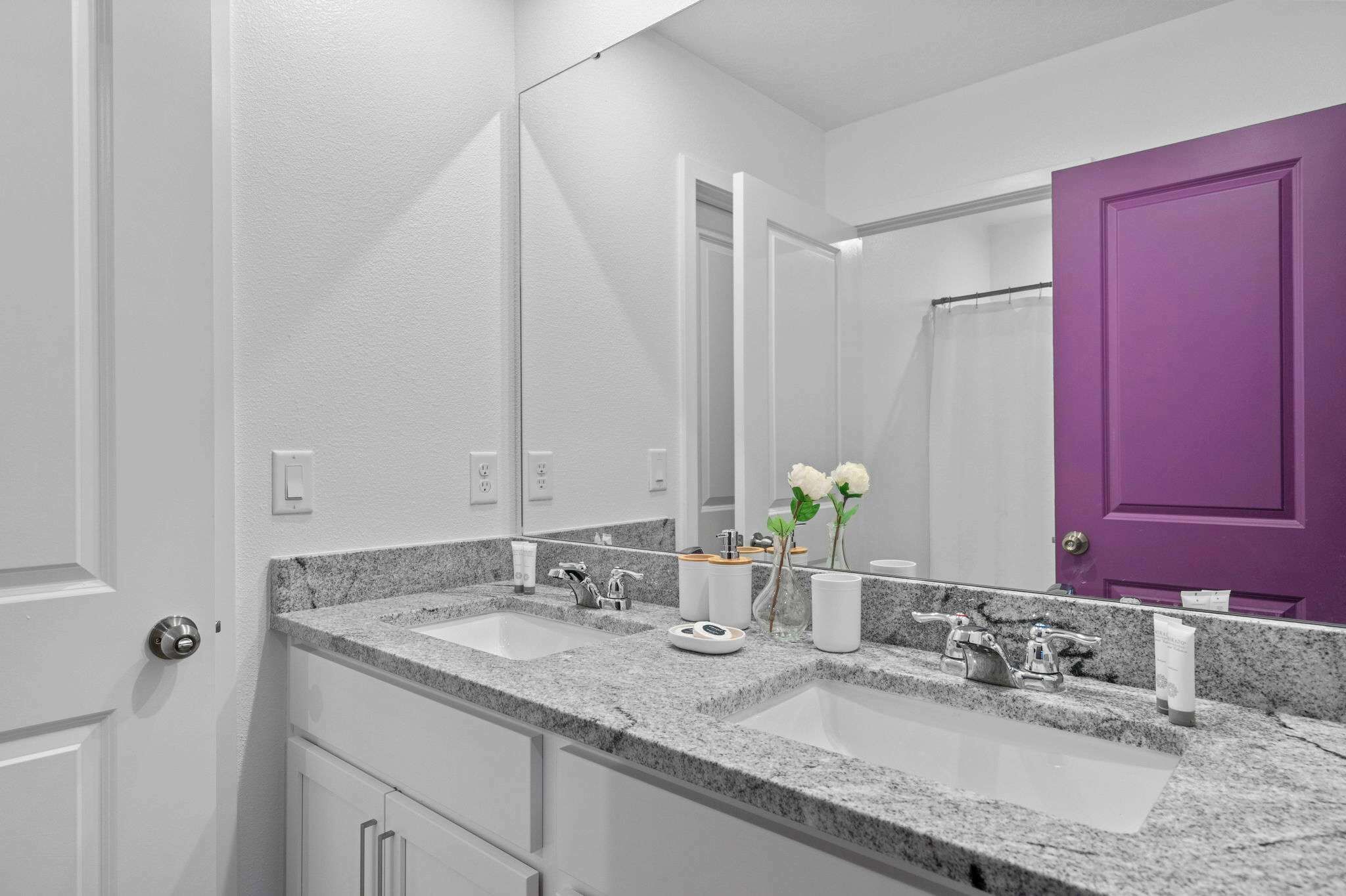 A bathroom with two sinks, a mirror, a purple door, and a white door.