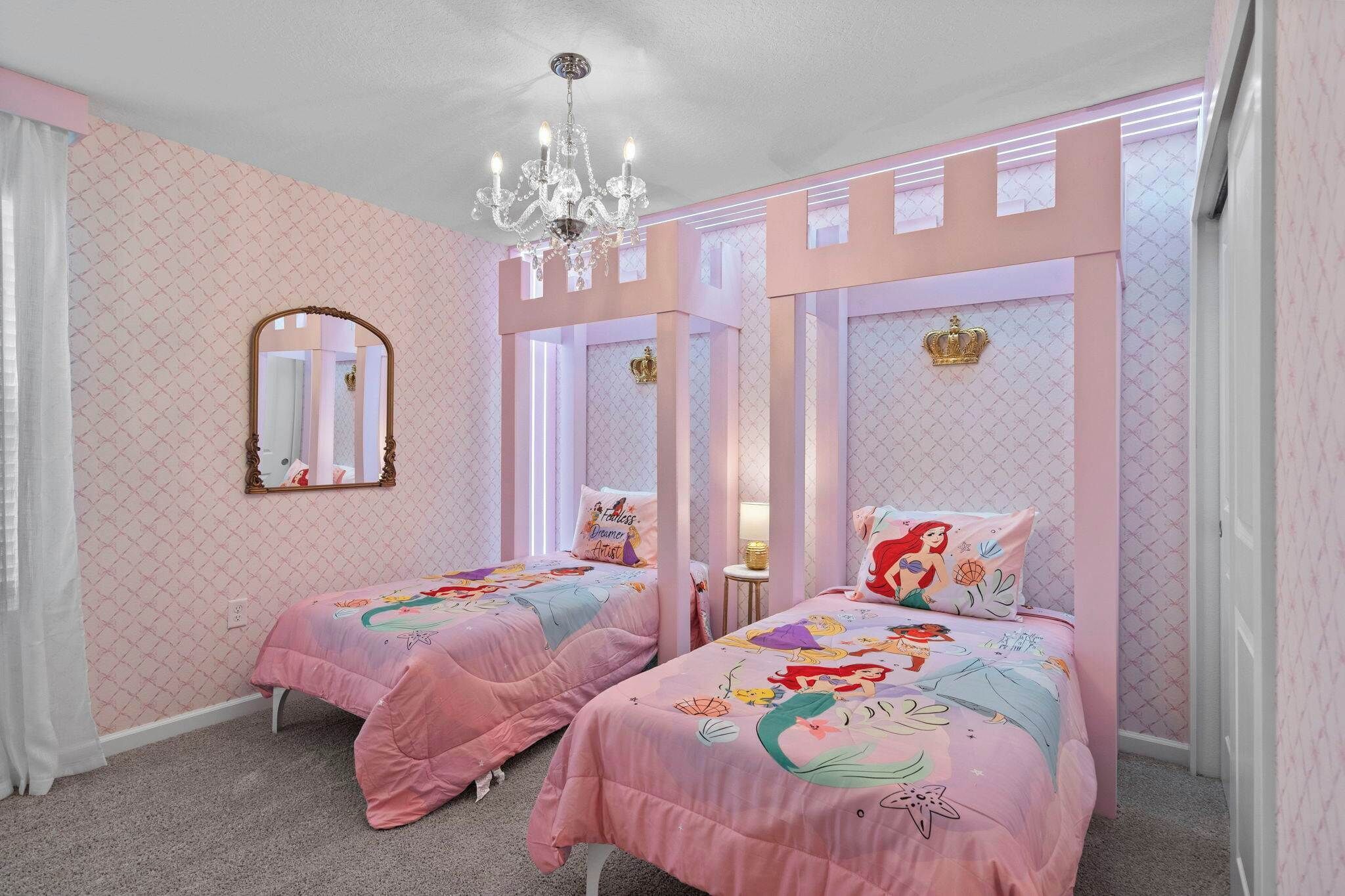 A bedroom with two beds, a chandelier, a mirror, and a crown decoration.