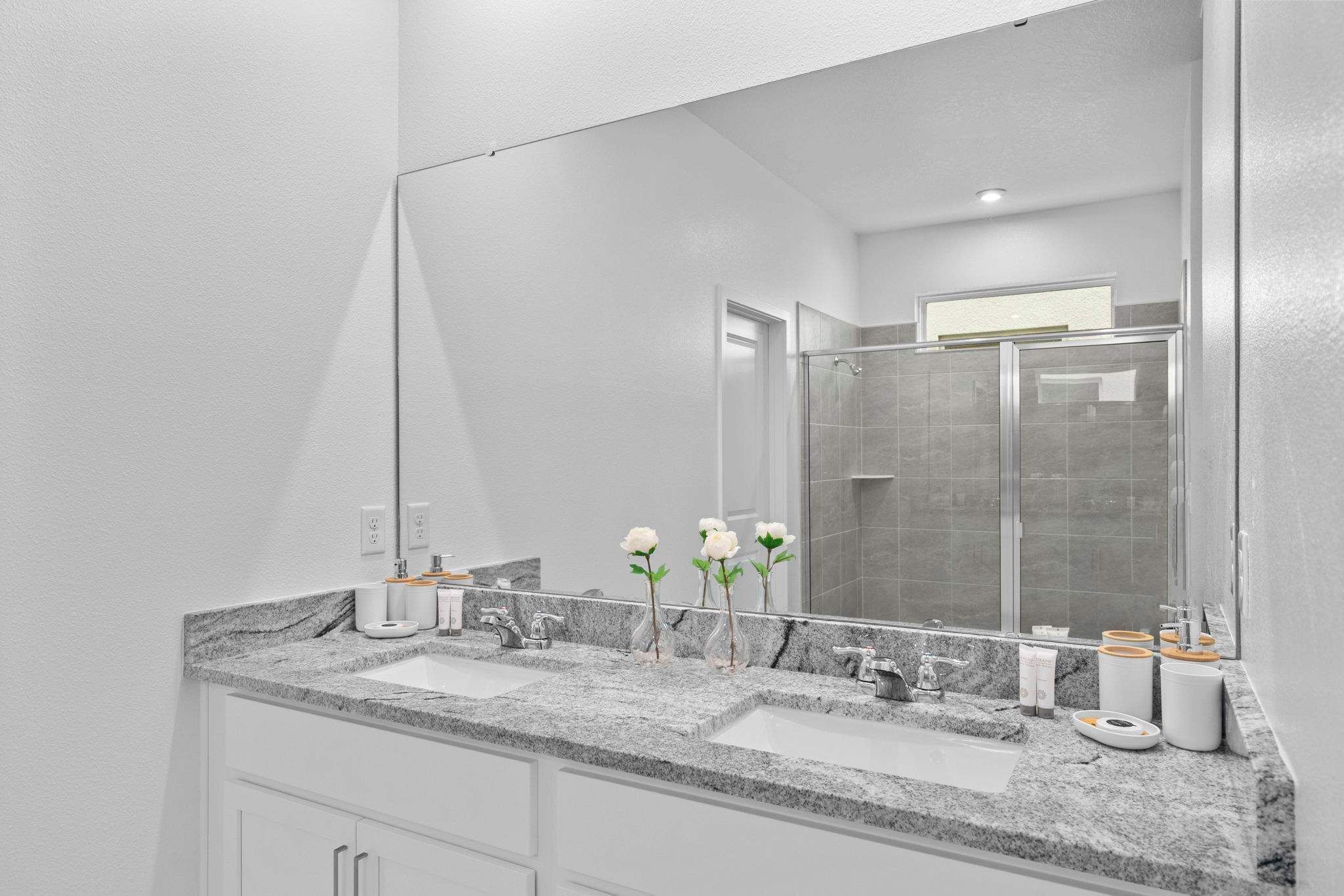 A modern bathroom with a large mirror, two sinks, and a shower area.