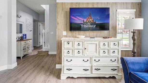 Ein Wohnzimmer mit einer weißen Kommode, einem an einer Holzwand montierten Flachbildfernseher und einem blauen Sessel.