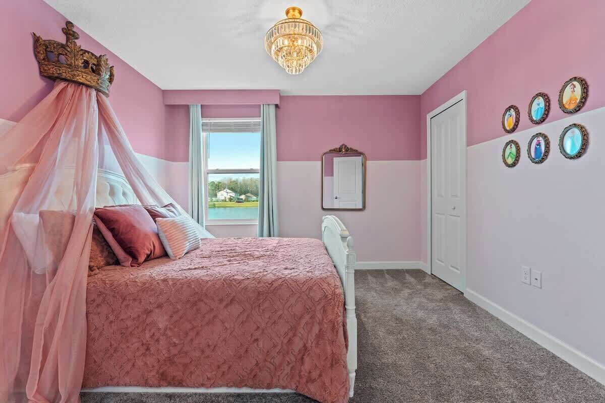 A bedroom with a canopy bed, a chandelier, a large window, and a door.