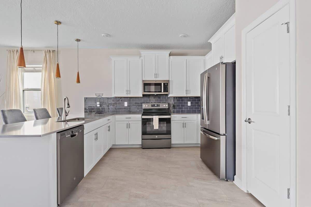 A modern kitchen with white cabinets, stainless steel appliances, and a tiled backsplash.