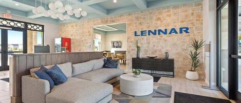 A modern lobby with a large LENNAR sign, a sectional sofa, a round coffee table, and a stone accent wall.