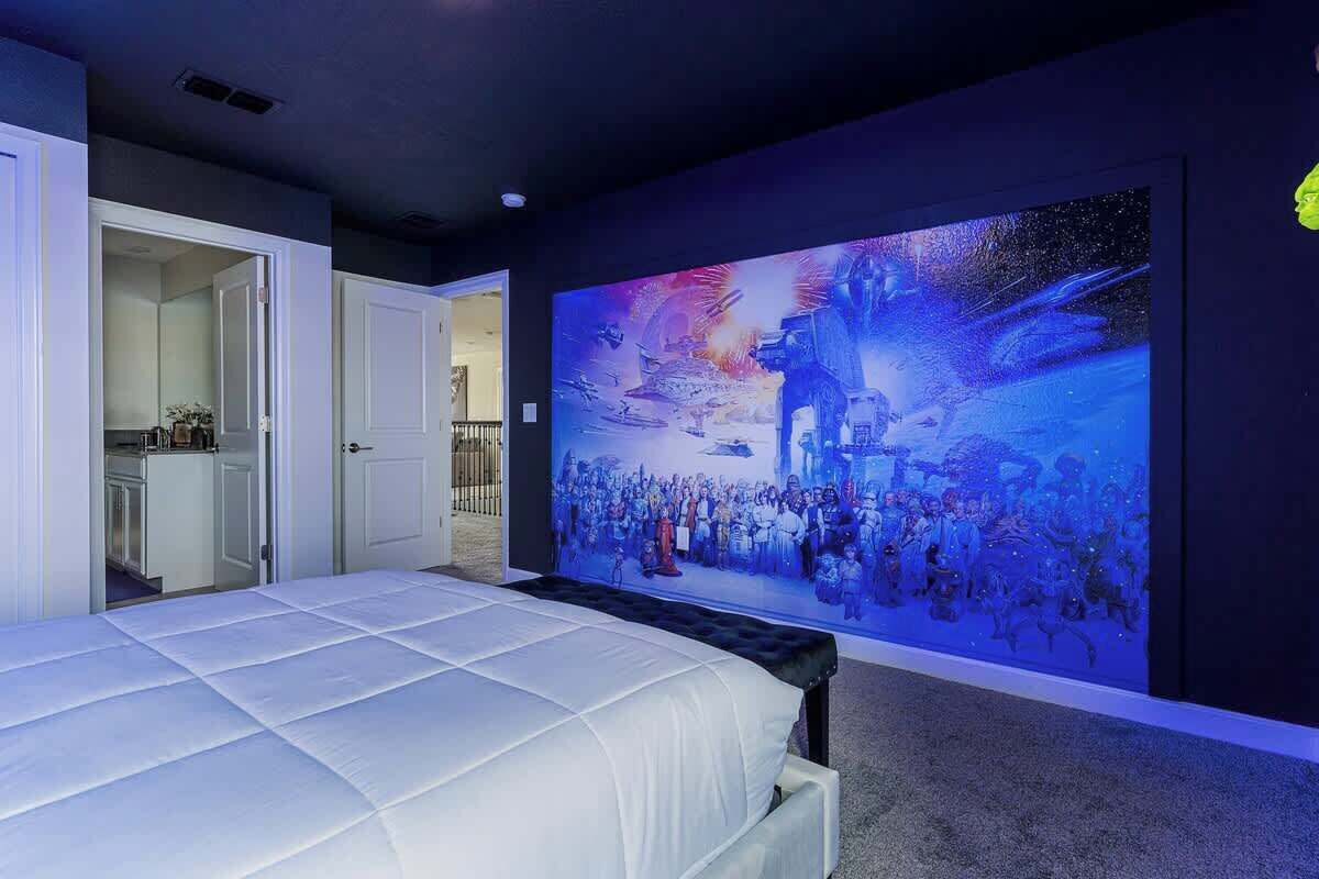 A bedroom with a large bed, a wall-mounted TV, and a door leading to a bathroom.