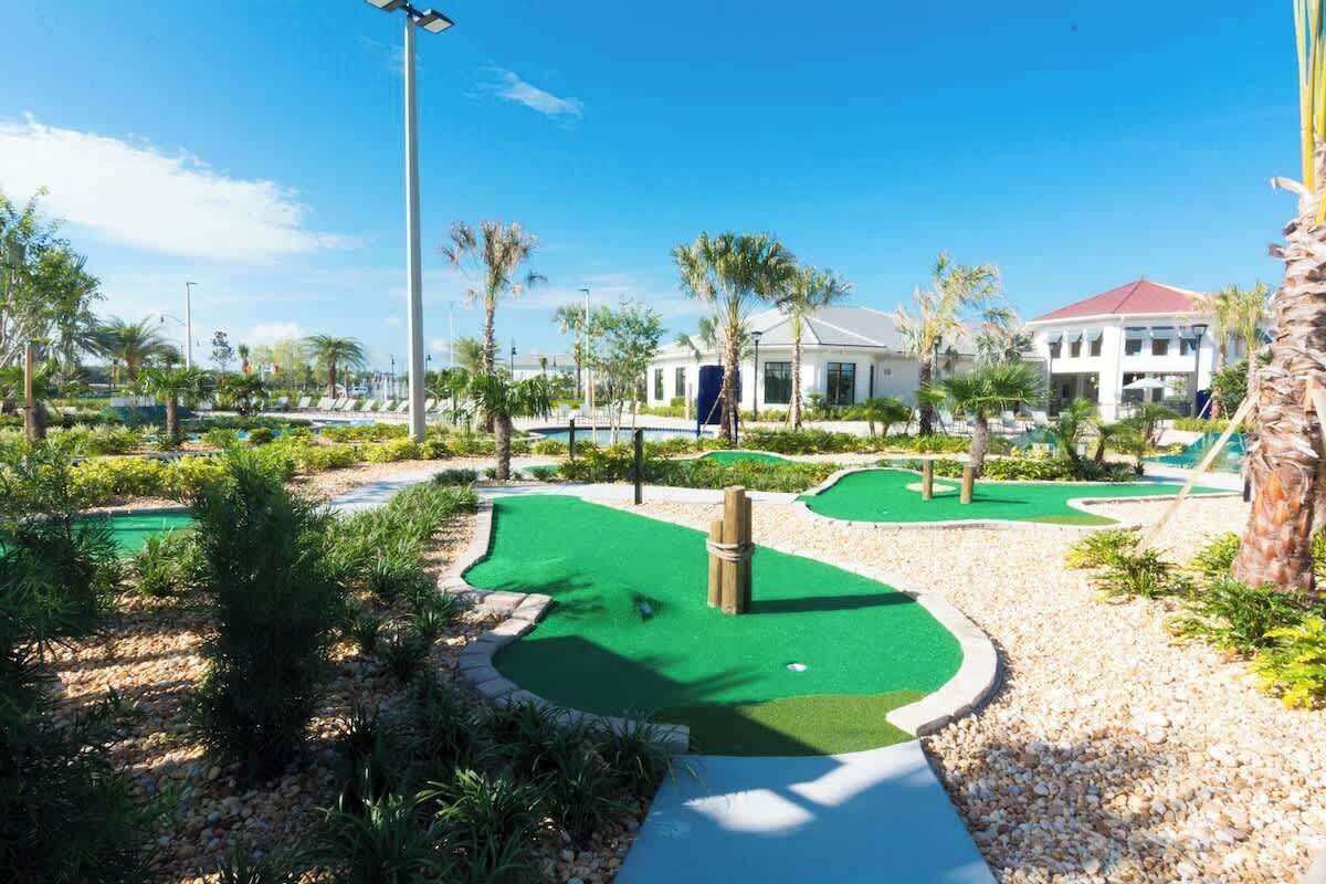 A golf course with multiple greens, palm trees, and a building in the background.