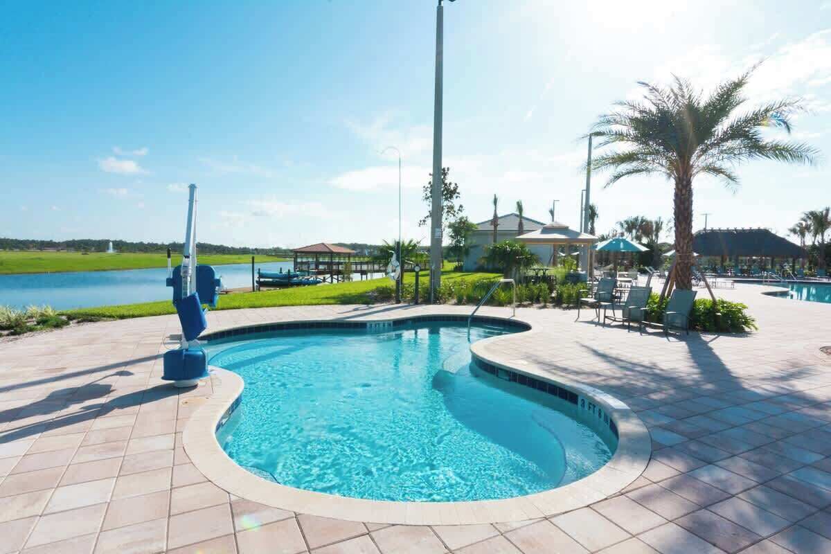 A swimming pool with a curved edge, surrounded by a tiled deck, palm trees, and a view of a body of water and buildings in the background.