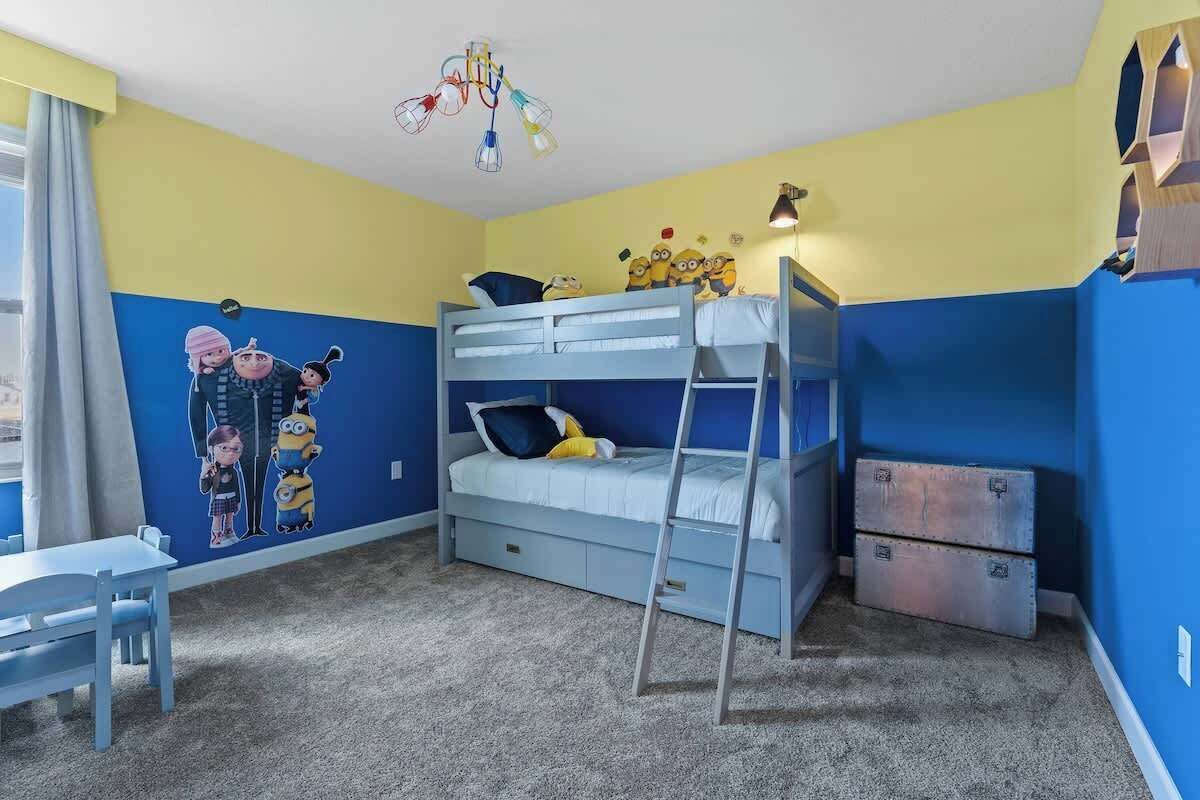 A child's bedroom with bunk beds, a desk, and a Minions mural on the wall.