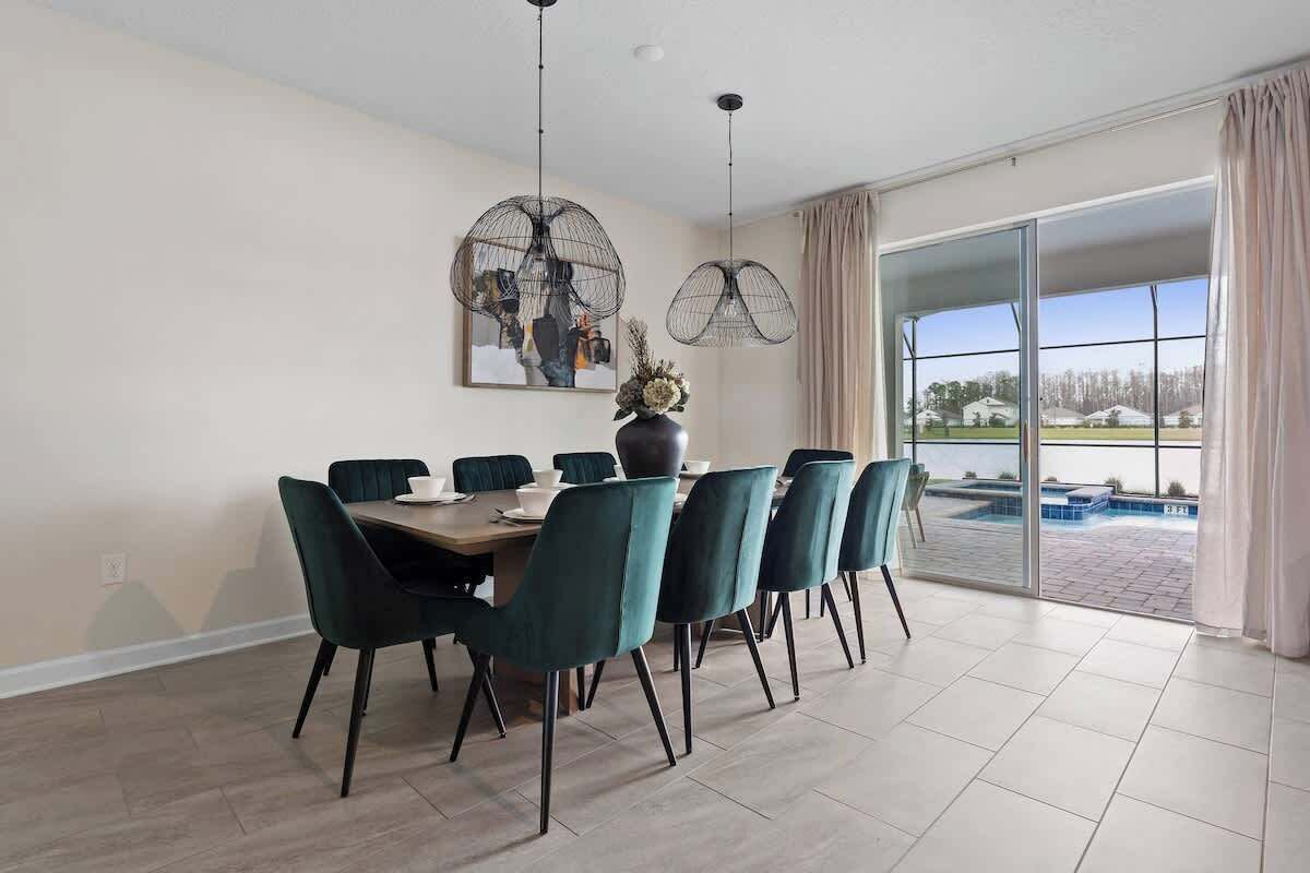 Un coin repas avec une table et des chaises, une grande fenêtre avec des rideaux et une vue sur une piscine.