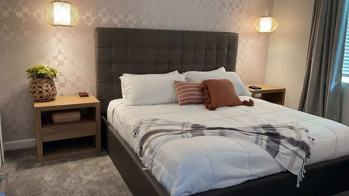 A modern hotel room with a large bed, two bedside tables, a decorative plant, and ambient lighting.