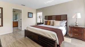Una camera da letto con un letto in legno, un comodino, una lampada e una porta che dà su un bagno.