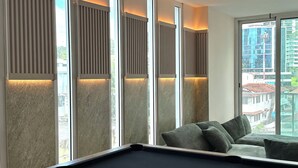A pool table with a set of balls, a sofa with cushions, and a view of a cityscape through large windows with vertical blinds. - Fabulous 5-bedroom apartment with AC in vibrant Panamá (Panamá)