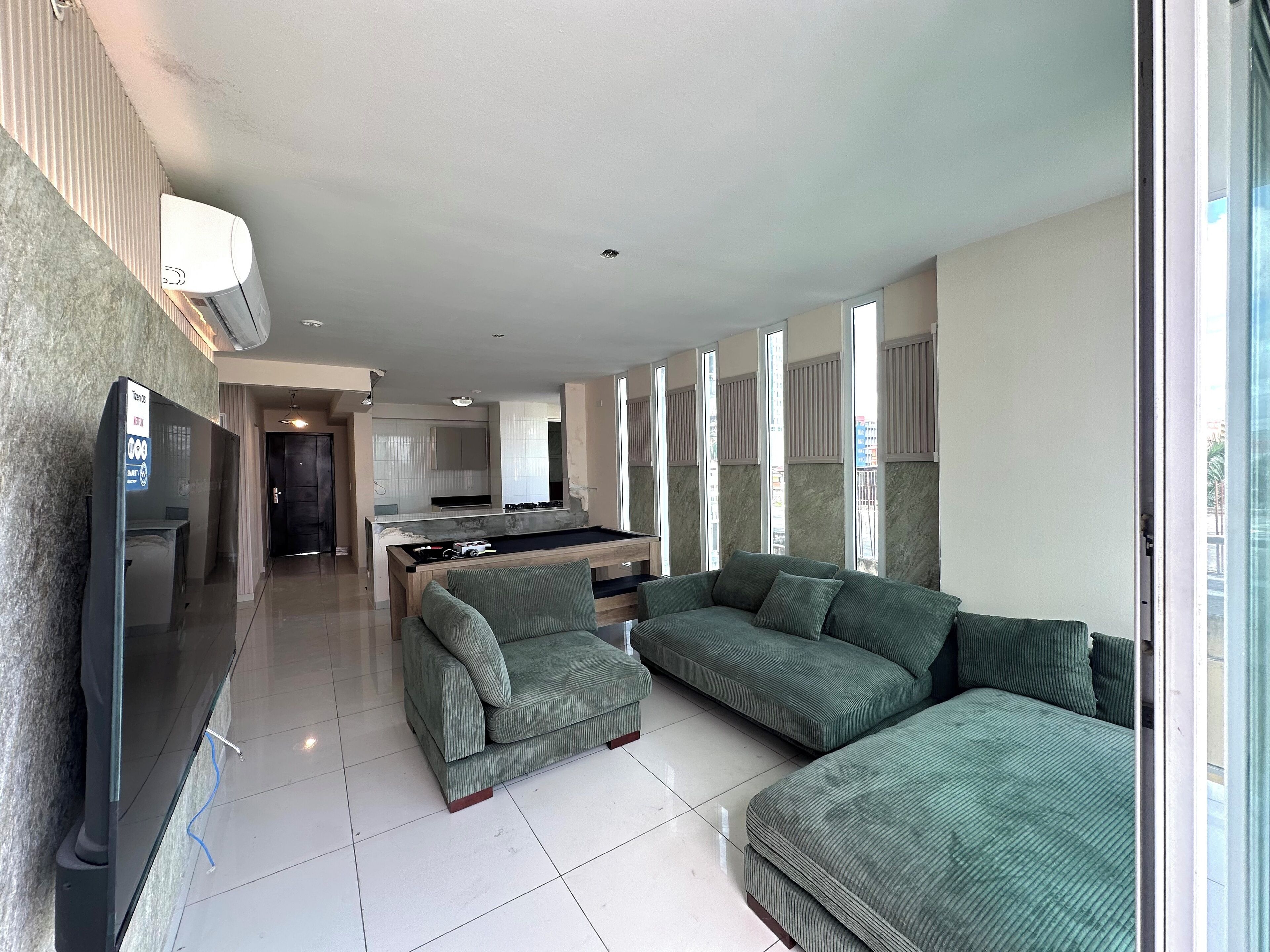 A spacious living area with a pool table, green sofas, and a flat-screen TV.
