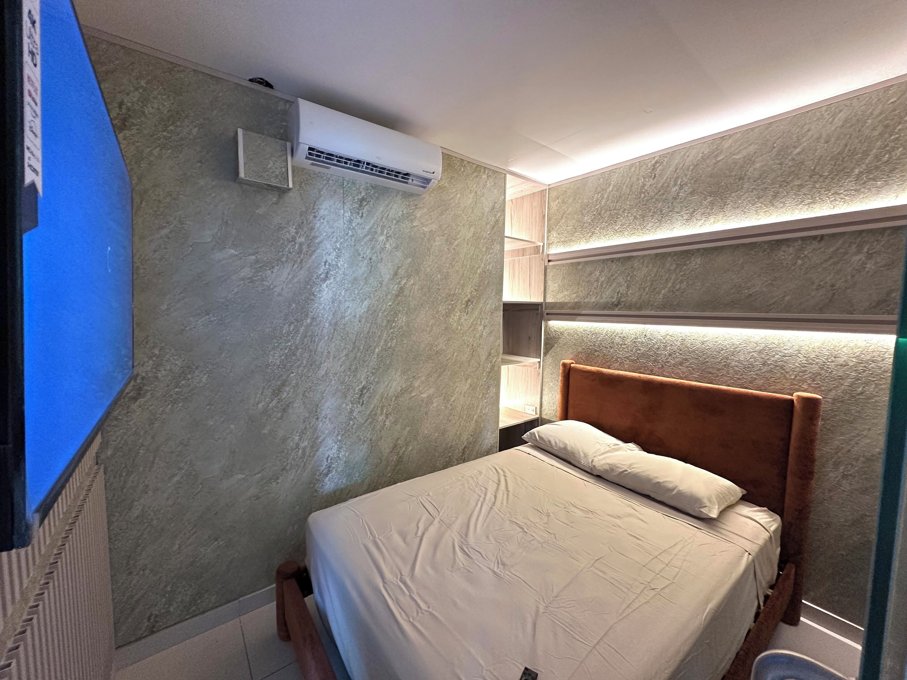 Un dormitorio con cama, aire acondicionado, repisa en la pared y mesita de noche.