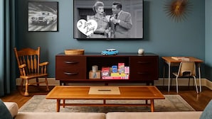 Ein Wohnzimmer mit Fernseher, Holzschrank, kleinem Tisch und einem blauen Automodell.