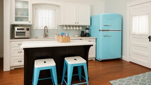 Eine Küche mit weißen Schränken, einem blauen Kühlschrank, einer weißen Arbeitsplatte und zwei blauen Barhocker.