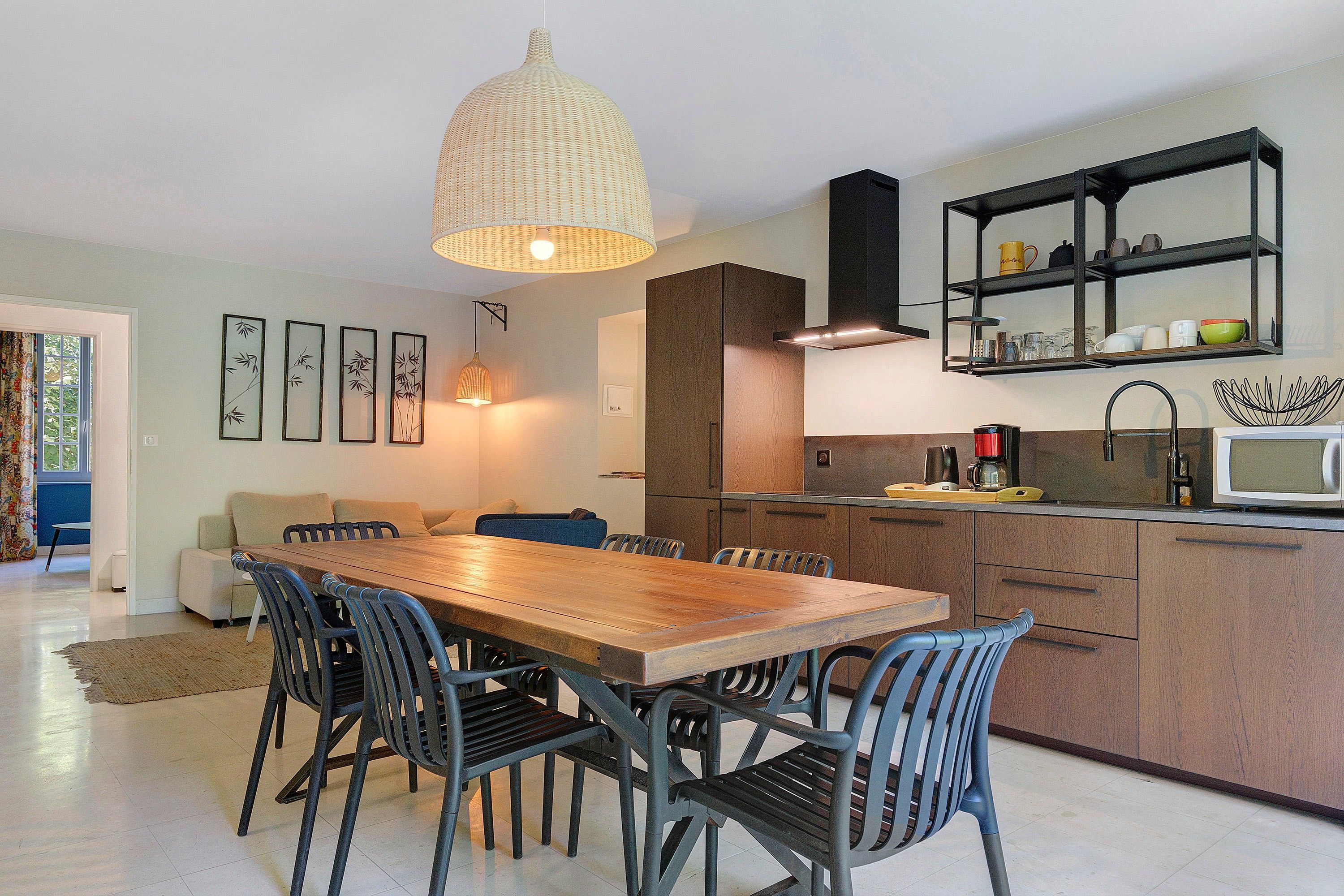 A modern kitchen with a wooden dining table, black chairs, and a hanging light fixture.