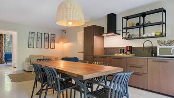 A modern kitchen with a wooden dining table, black chairs, and a hanging light fixture.