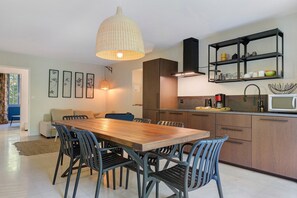 A modern kitchen with a wooden dining table, black chairs, and a hanging light fixture. - Apartment 'Gîte Simone' with Mountain View, Private Pool and Wi-Fi (Vallon-Pont-d'Arc)