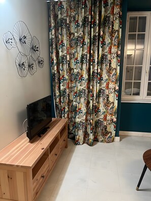 Een kamer met een televisie op een houten standaard, een gordijn met een traditioneel patroon en een muur met een geometrisch ontwerp.