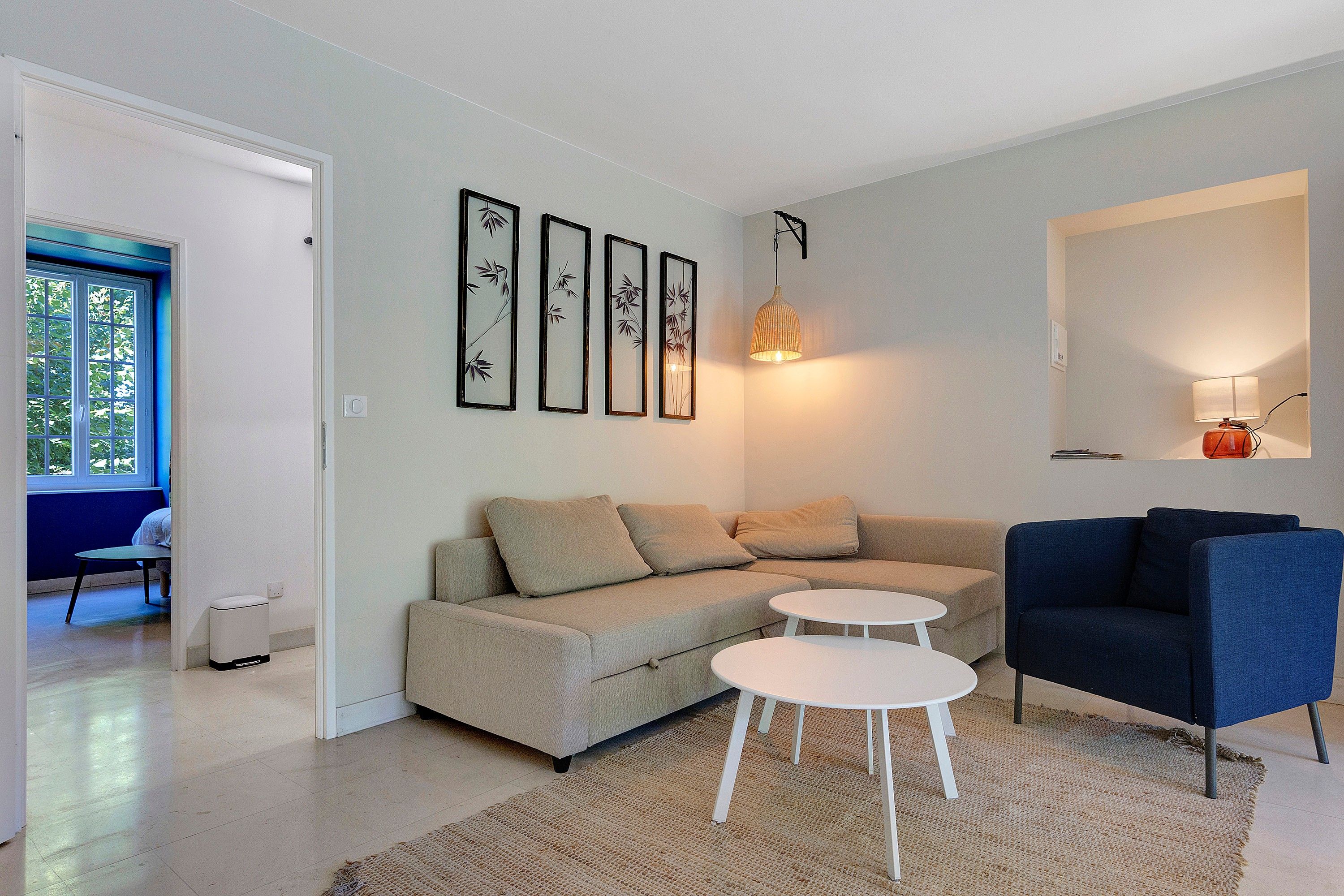 Ett modernt vardagsrum med en soffa, två sidobord, en blå fåtölj och en hängande lampa.