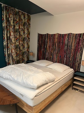 Un dormitorio con cama, cortinas, una mesita de noche y una lámpara.