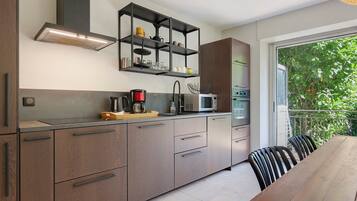Cozinha moderna com eletrodomésticos embutidos, área de jantar com mesa de madeira e vista para o verde através de uma porta de vidro.