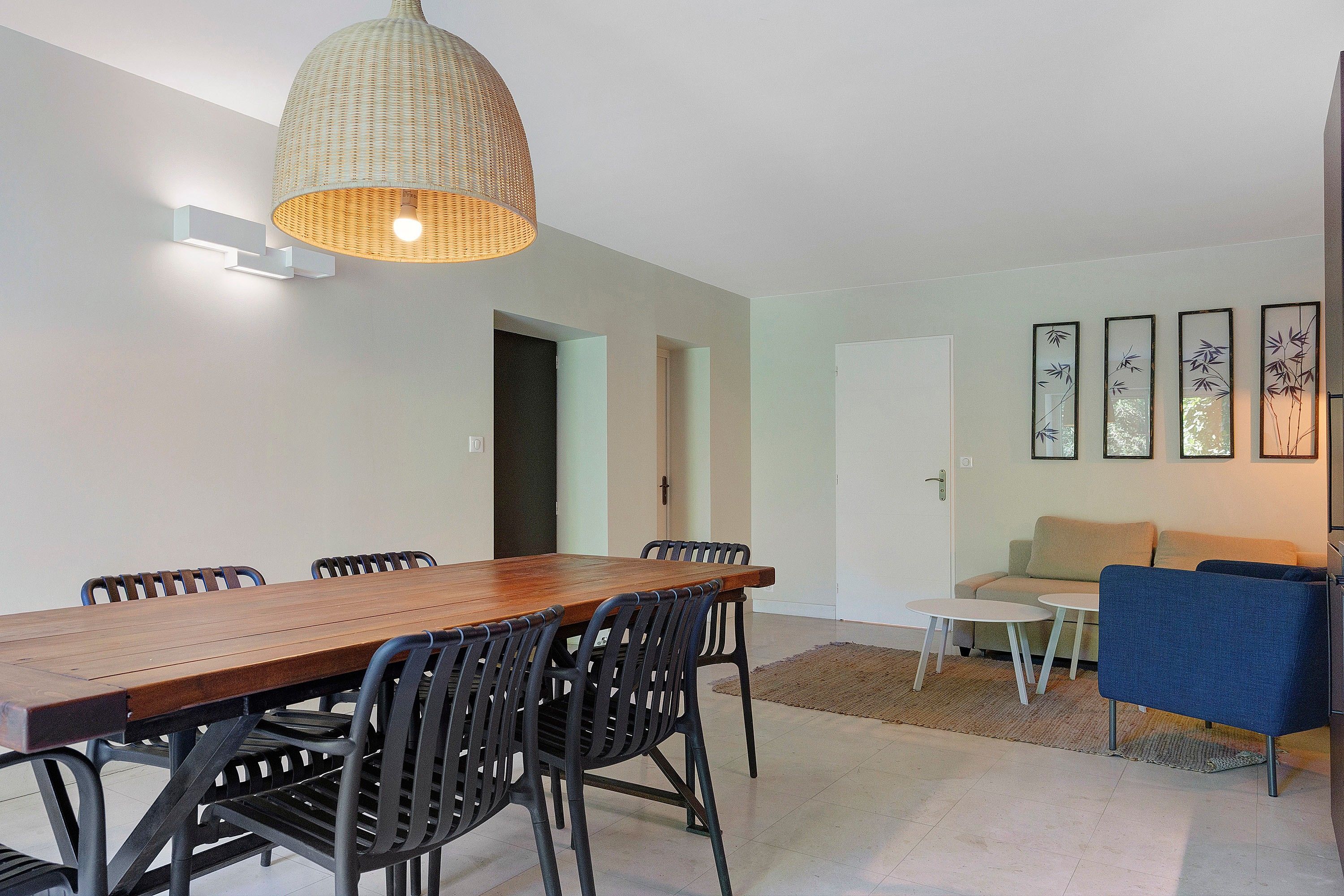 Een moderne eethoek met een houten tafel en stoelen, een hanglamp en een zithoek met een bank en wanddecoratie.