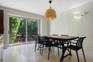 A dining area with a large table and chairs, a sliding glass door leading to a balcony, and a hanging light fixture.