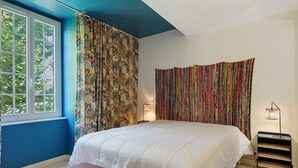 Een slaapkamer met een groot bed, een raam met gordijnen, een bedlampje en een klein tafeltje.