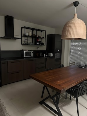 Cozinha moderna com armários escuros, uma mesa de jantar de madeira e um lustre.
