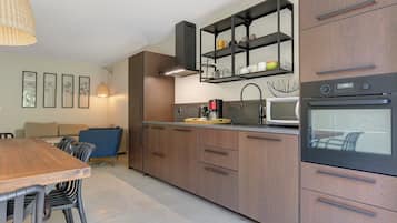 A modern kitchen with wooden cabinets, a built-in oven, and a dining area with a table and chairs.