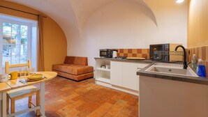 A compact kitchen with a dining area, a sofa, and a window with curtains.