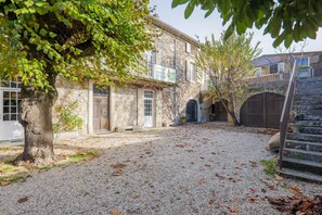 Un edificio de piedra con un patio de grava, un árbol y una escalera que lleva a una puerta.