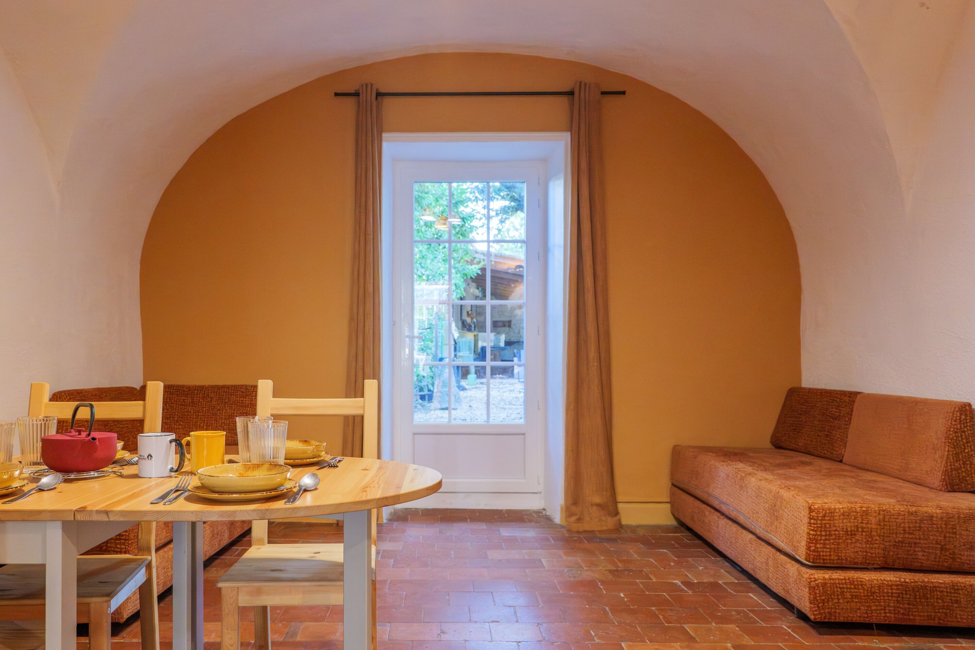 Un coin repas avec une table dressée pour quatre personnes, un canapé et une porte donnant sur l’extérieur.