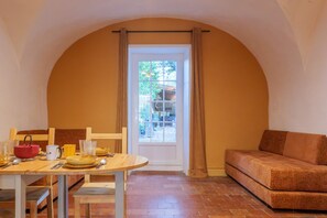 Un coin repas avec une table dressée pour quatre personnes, un canapé et une porte donnant sur l’extérieur.