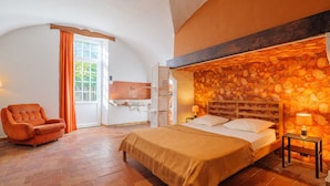A bedroom with a bed, a chair, a TV, and a stone wall.