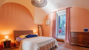 A bedroom with a bed, bedside table, lamp, dresser, and a window with curtains.