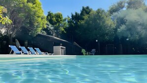 A swimming pool with clear water, surrounded by trees and a building with a covered area. - Gîte Yves Apartment with Park View, Private Pool, and Wi-Fi (Vallon-Pont-d'Arc)