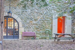 Een stenen muur, een houten bank, een picknicktafel en een deur met een oranje binnenkant.