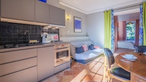 A compact kitchen with a stove, oven, and sink, a dining area with a table and chairs, and a sofa in the living area.