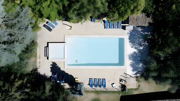 Vista aérea de uma piscina com espreguiçadeiras, um deck e vegetação ao redor.