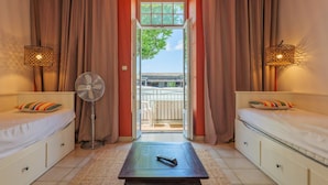 Une chambre avec deux lits, un ventilateur, une télécommande et une vue sur l’extérieur par une fenêtre.