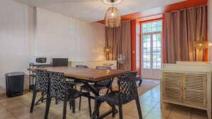 Un coin repas avec une table en bois, des chaises noires, un ventilateur de plafond, un four à micro-ondes et une fenêtre avec des rideaux.