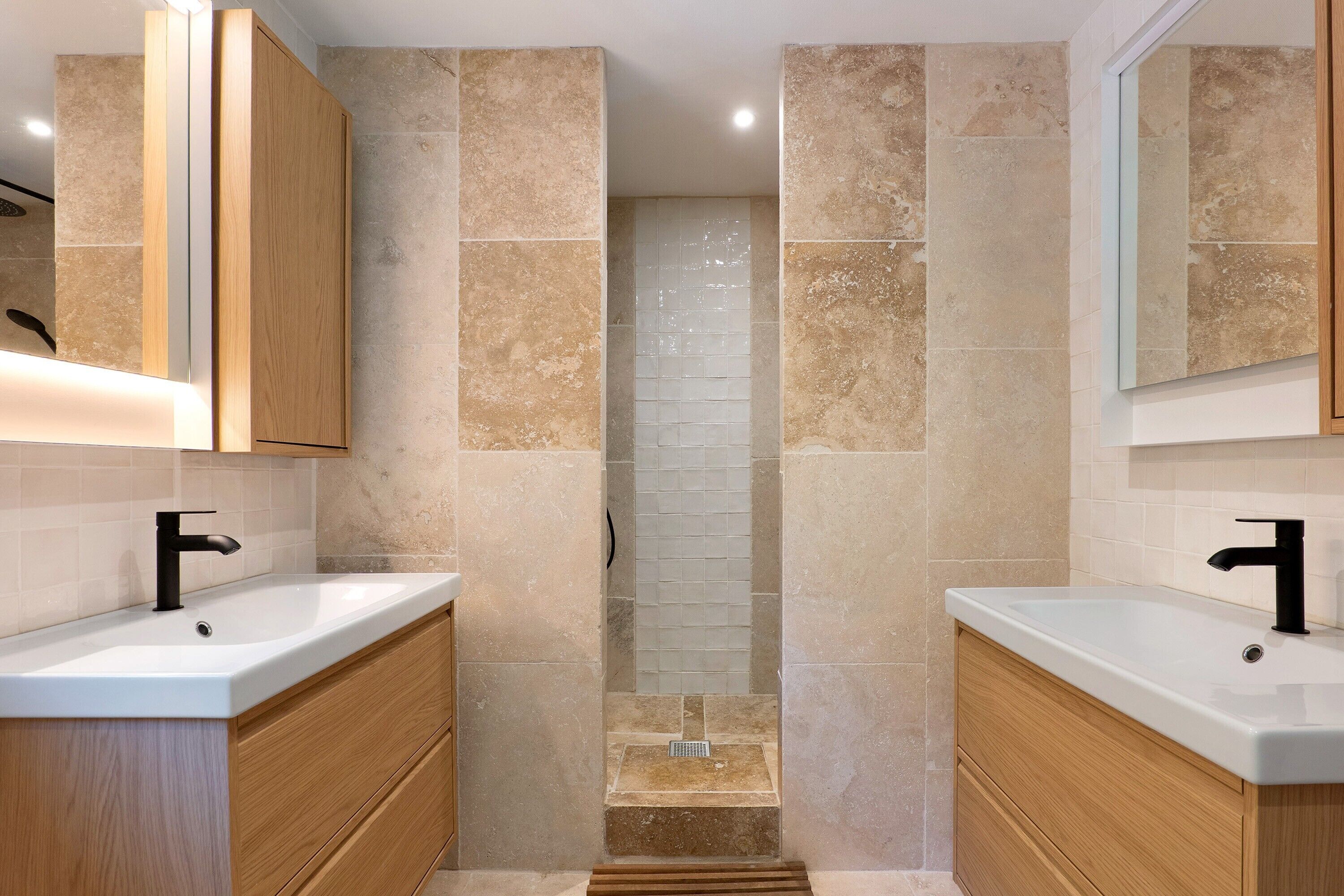 Un baño moderno con dos lavamanos, armarios de madera y zona de ducha.