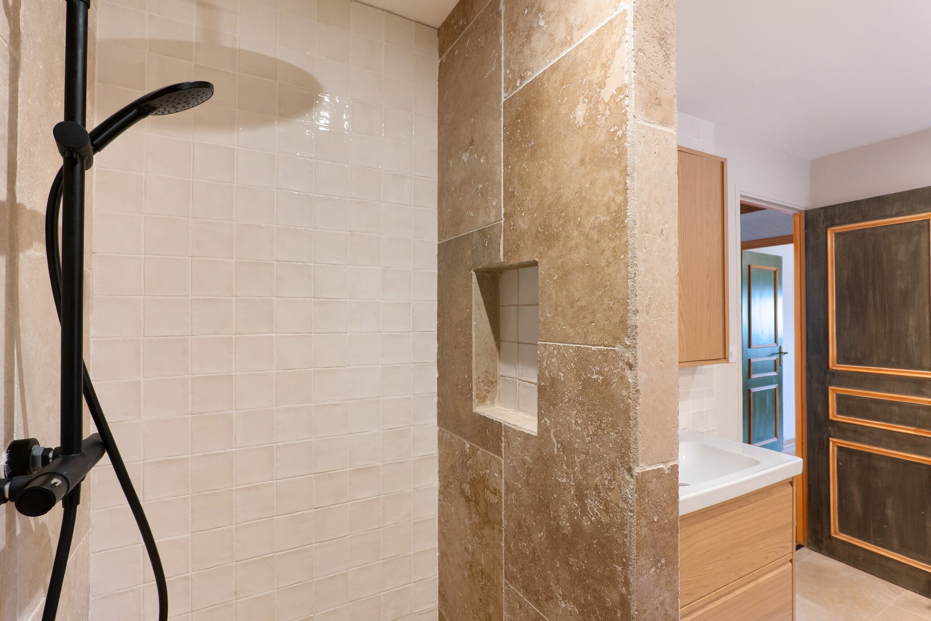 Une salle de bain avec douche, murs carrelés, un mur d’accent en marbre et des meubles en bois.