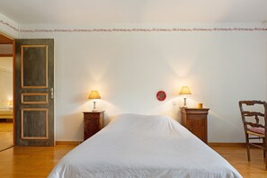 Um quarto com uma cama, duas mesas de cabeceira com luminárias, uma cadeira e uma porta.