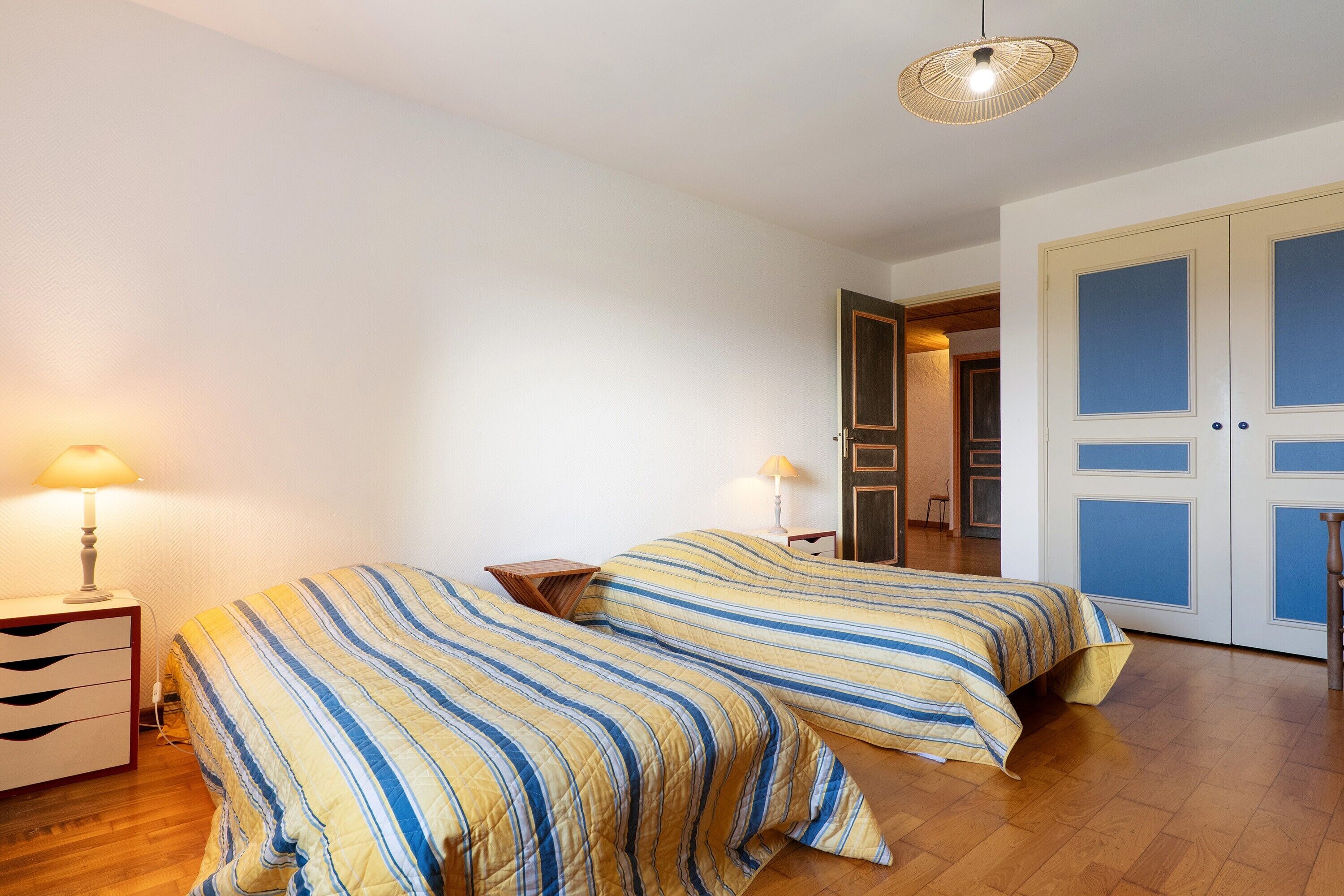 A bedroom with two beds, a nightstand, a lamp, and a door.